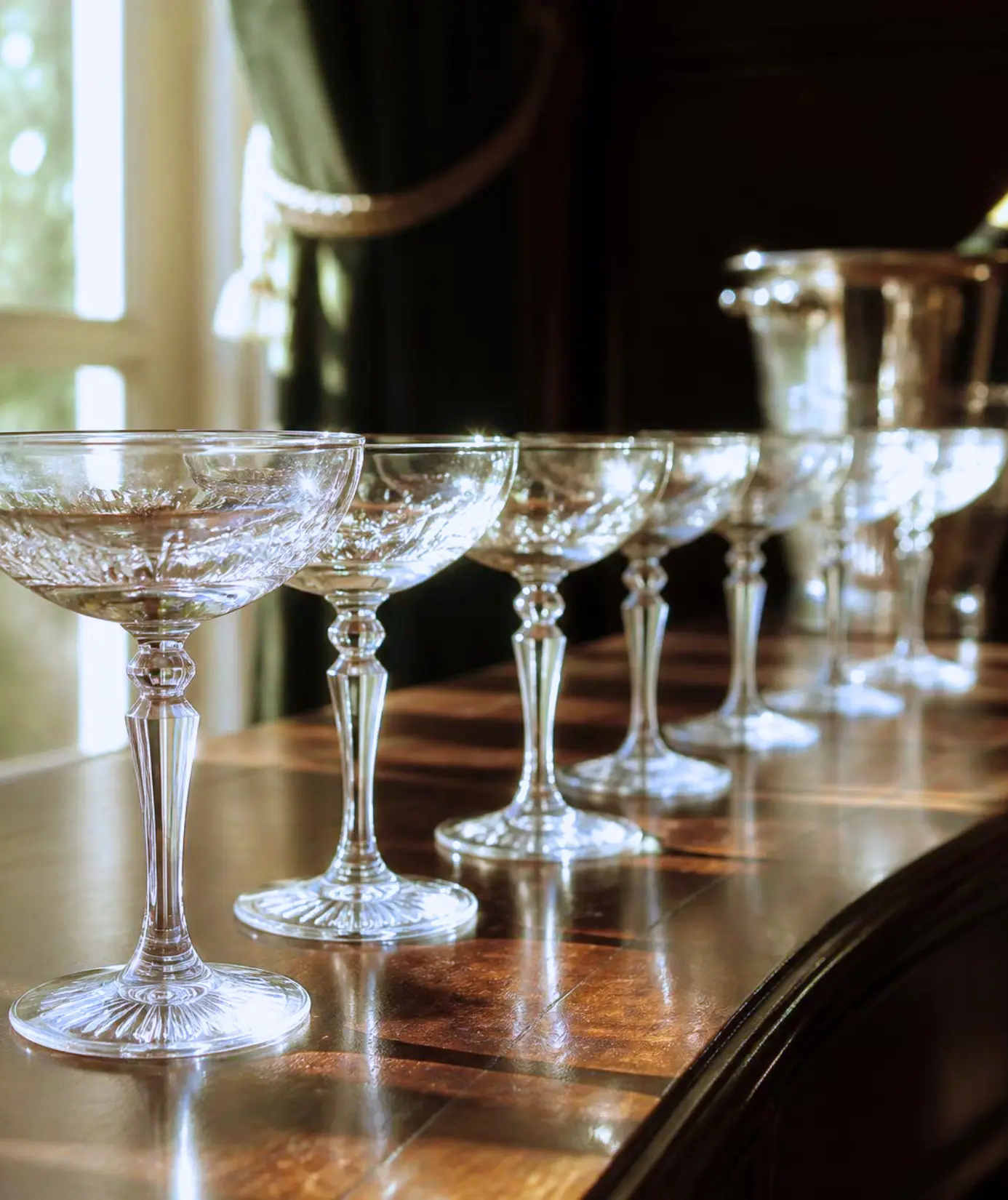 Row of vintage crystal coupe glasses on a polished wood bar in warm light